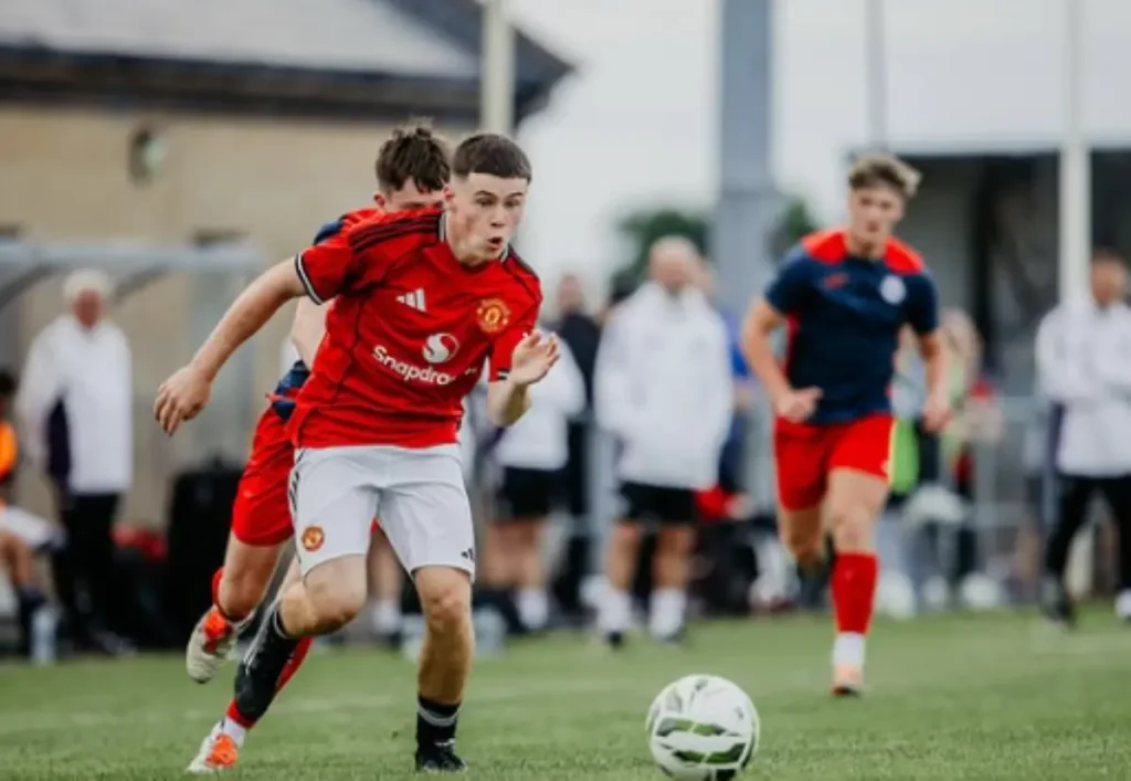Kai Rooney bermain di pertandingan Manchester United U16 melawan tim lawan, berlari mengejar bola di lapangan.
