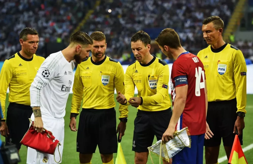 Mark Clattenburg memimpin undian koin antara Sergio Ramos dan Gabi di Final Liga Champions 2016 antara Real Madrid dan Atletico Madrid.