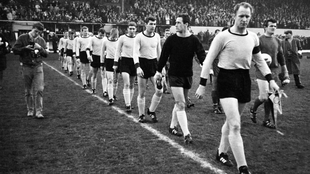 Skuad Borussia Dortmund berjalan di lapangan pada final European Cup Winners' Cup 1966 melawan Liverpool, momen bersejarah yang membuat mereka mengenal lagu You'll Never Walk Alone.