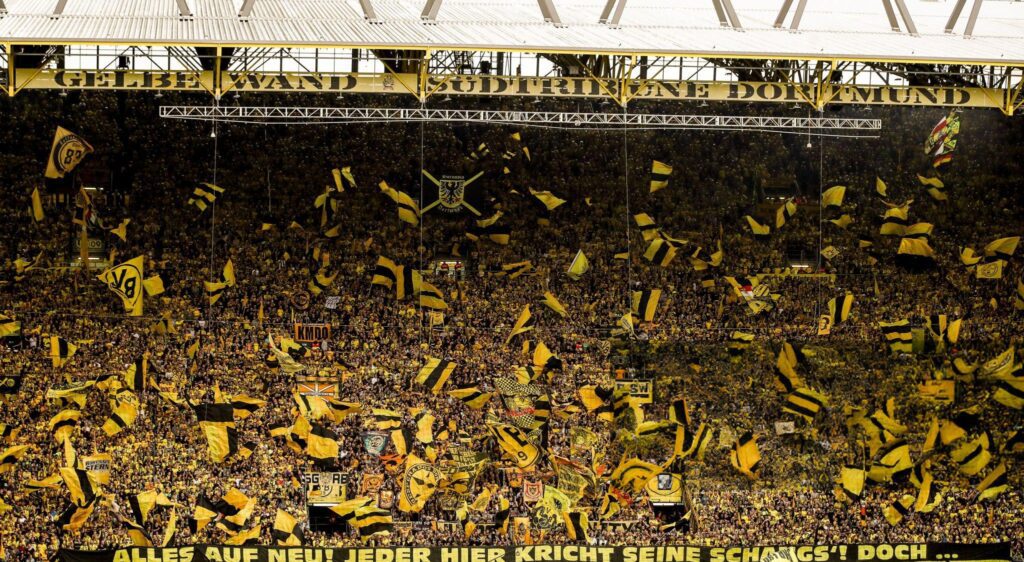 ribun Selatan atau Yellow Wall Borussia Dortmund dipenuhi ribuan fans dengan bendera kuning-hitam, menciptakan atmosfer megah saat You'll Never Walk Alone berkumandang.